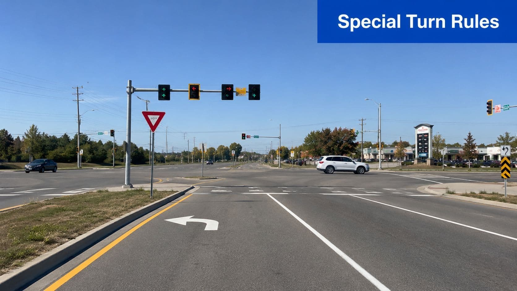 A view of an intersection with traffic lights, turn lanes, and road signs under a clear blue sky.